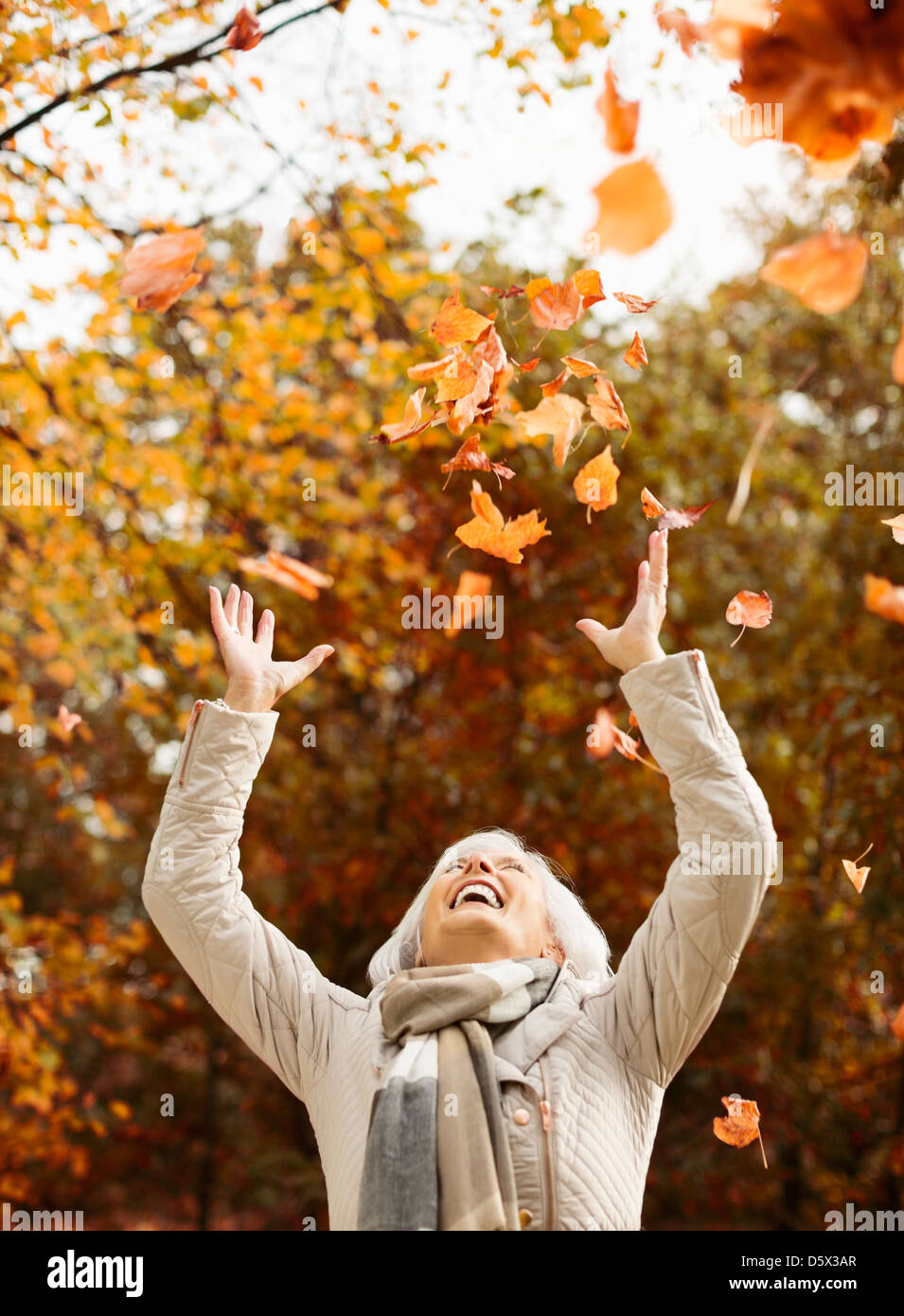 Femme plus âgée, jouant dans les feuilles d'automne Banque D'Images