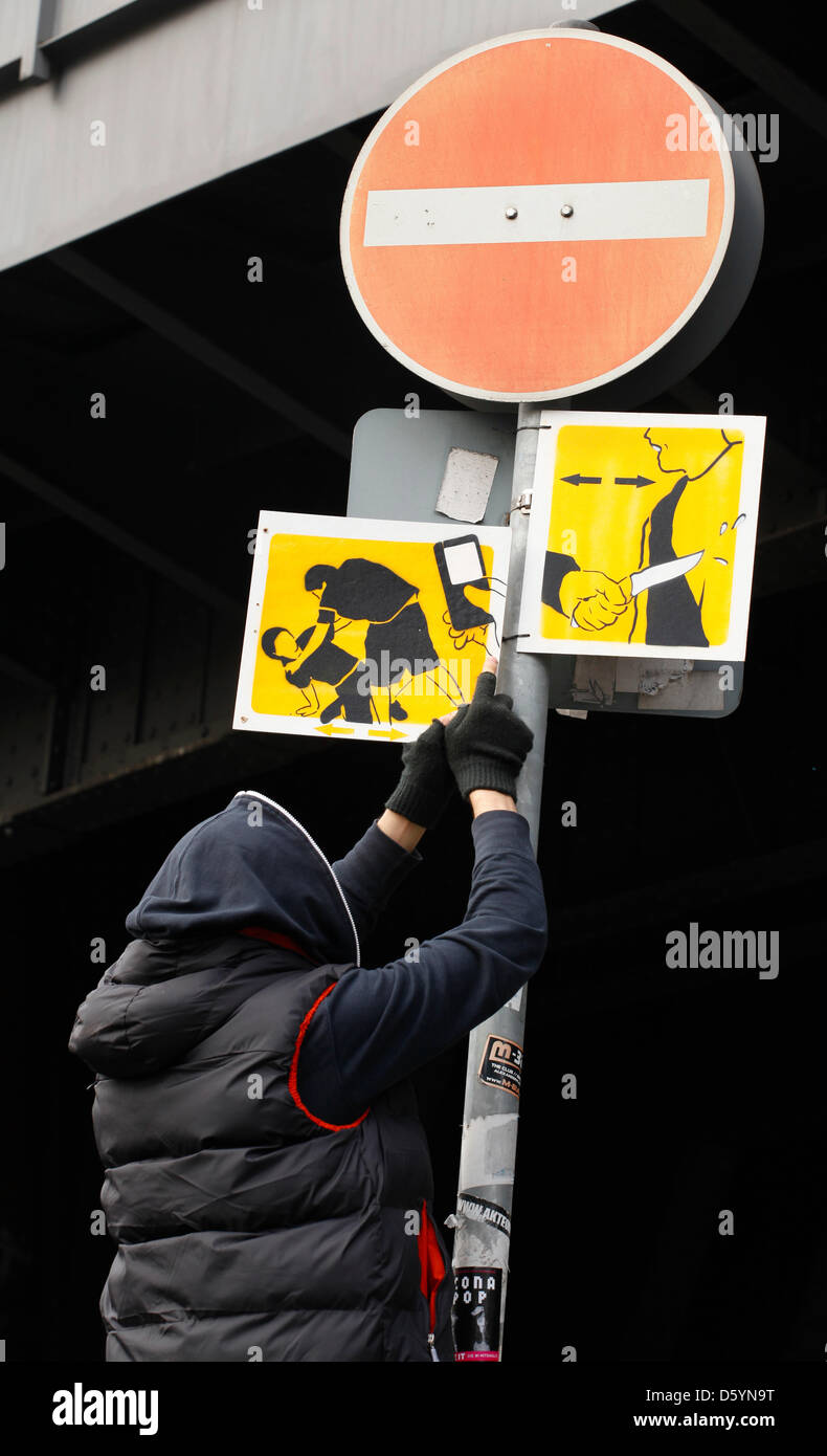 Artiste El Bocho démontre comment il attache un de ses pictogrammes pour un poteau de signalisation à Berlin, Allemagne, 31 octobre 2012. La photo présente une scène où quelqu'un est battu pendant que quelqu'un filme la scène avec un téléphone mobile. Strett El Bocho artiste de Berlin a commencé un art d'action contre la violence dans les grandes villes, le 31 octobre 2012. Il a l'intention de mettre en place plus de 250 pictogrammes Banque D'Images