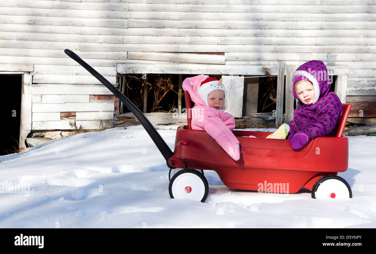 Fille avec petite Sœur assis dans Toy chariot Push Banque D'Images