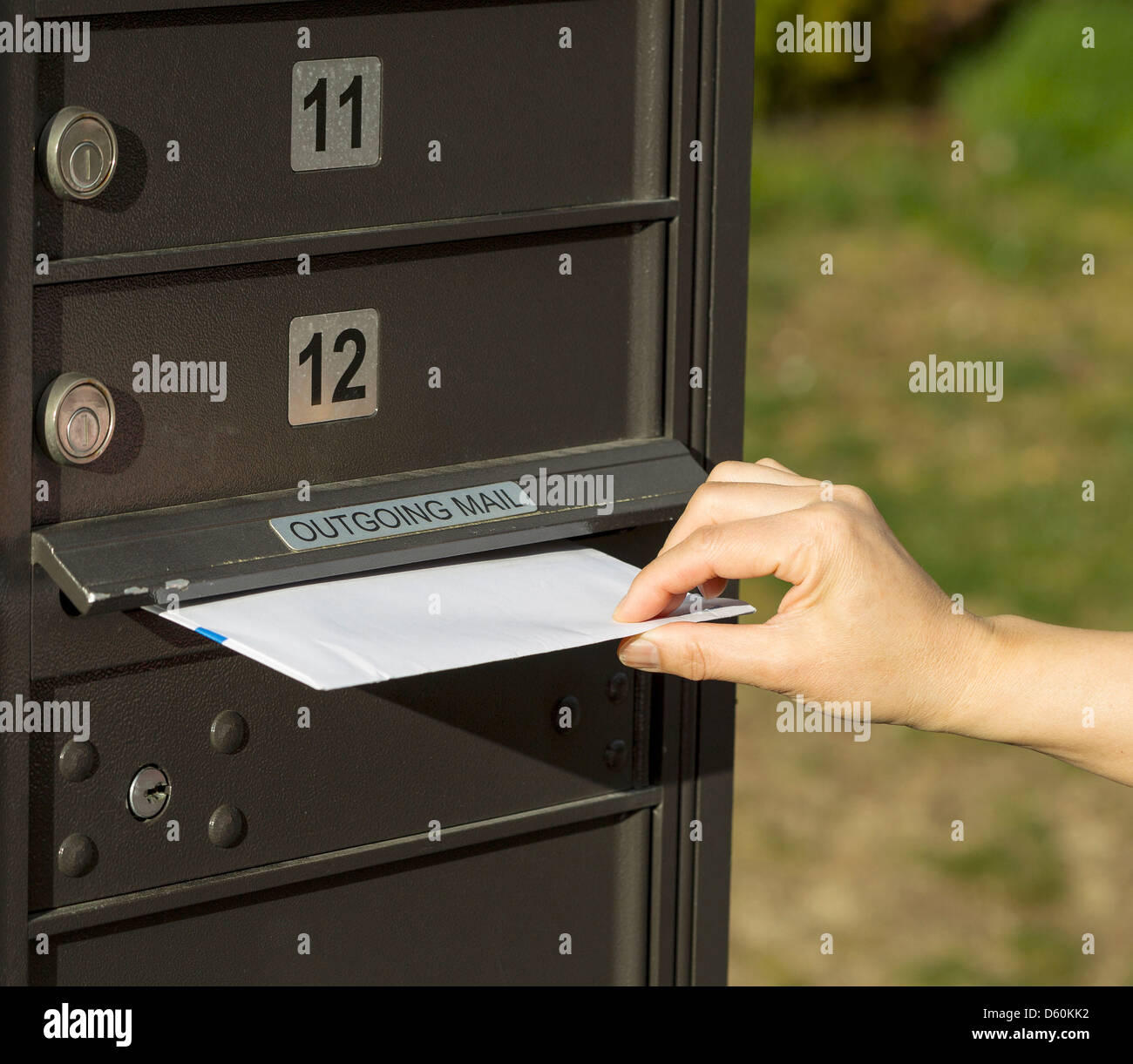 Photo de femme part mettre lettre dans la boîte aux lettres postale sortant avec l'herbe verte en arrière-plan Banque D'Images