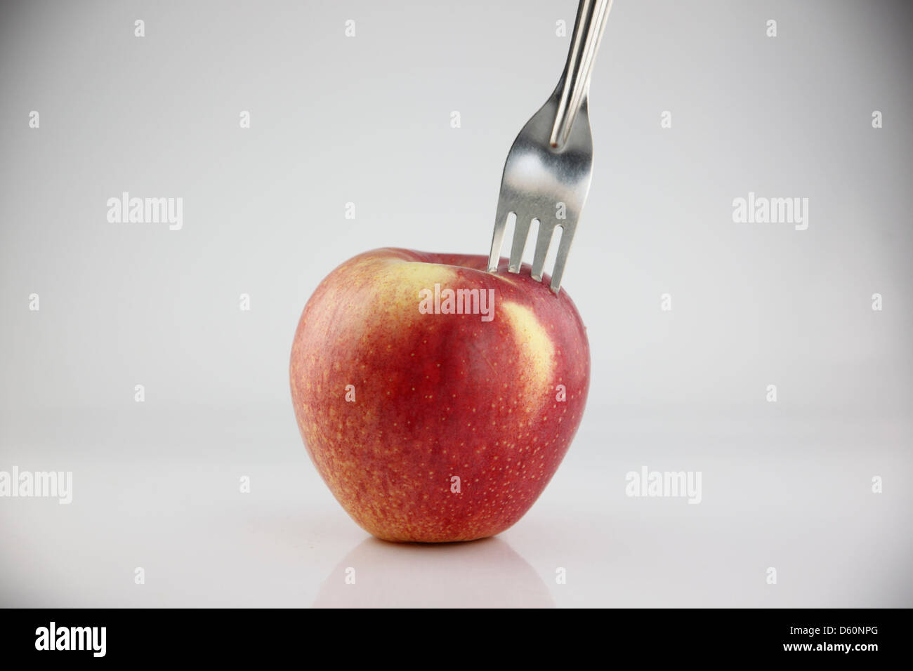 La Pomme Rouge sur le fond blanc, le Red Apple il y a une fourchette dans elle. Banque D'Images
