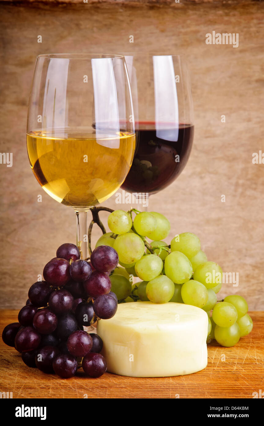 La vie encore la composition avec du vin rouge et blanc, les raisins et le fromage sur un arrière-plan vintage en bois Banque D'Images