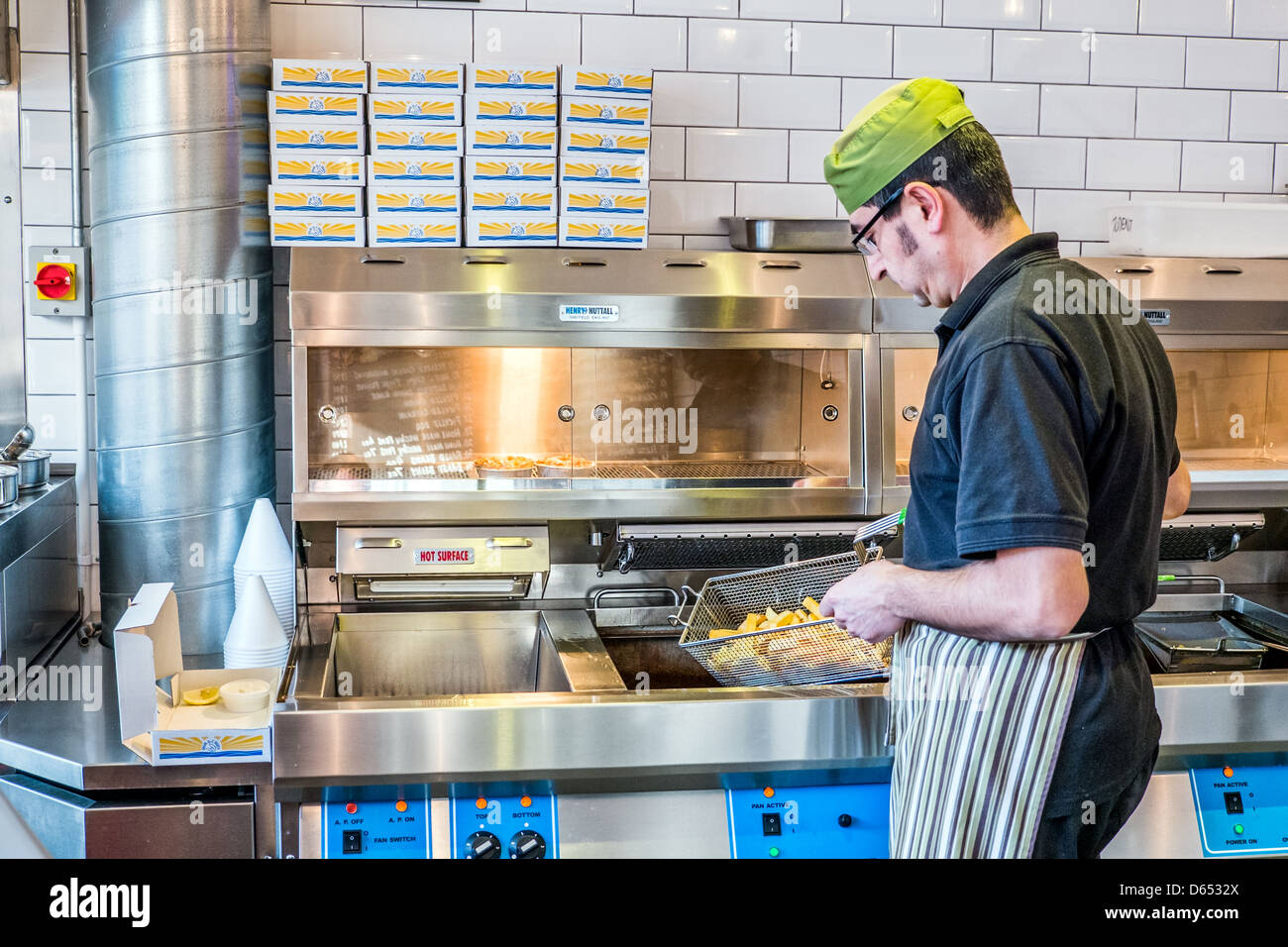 Un homme la cuisson du poisson et des frites dans un poisson traditionnel britannique et chip shop Banque D'Images