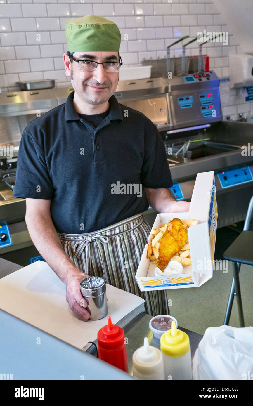 Un homme qui sert du poisson et des frites dans un poisson traditionnel britannique et chip shop Banque D'Images