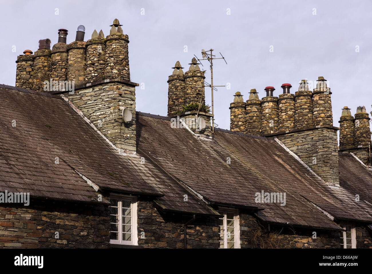 Cheminées carrées en pierre sèche en ardoise et pots ronds au-dessus des toits en terrasse de lakeland Cottage, Skelwith, Cumbria, Angleterre, Royaume-Uni Banque D'Images