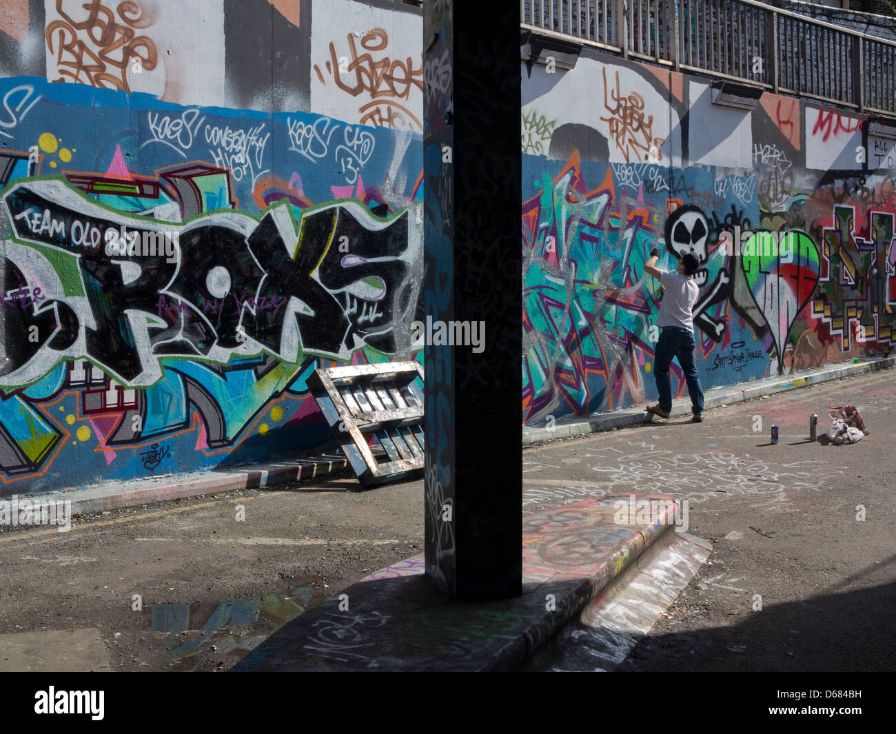 Jeune homme spray graffiti sur un mur dans un tunnel à Leake Street. London UK. La zone est réservée aux artistes de graffiti Banque D'Images
