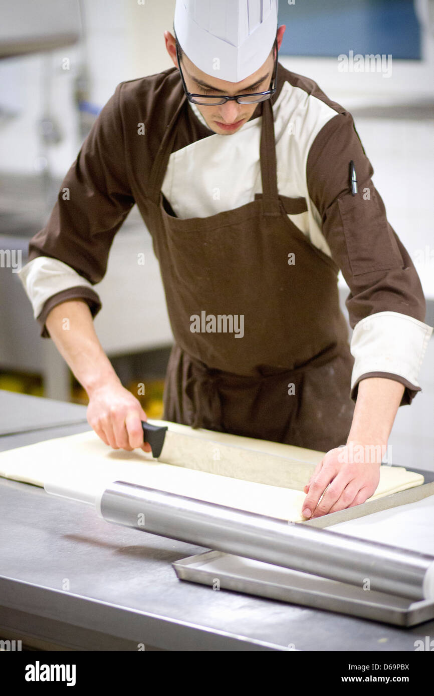Baker slicing dough in kitchen Banque D'Images