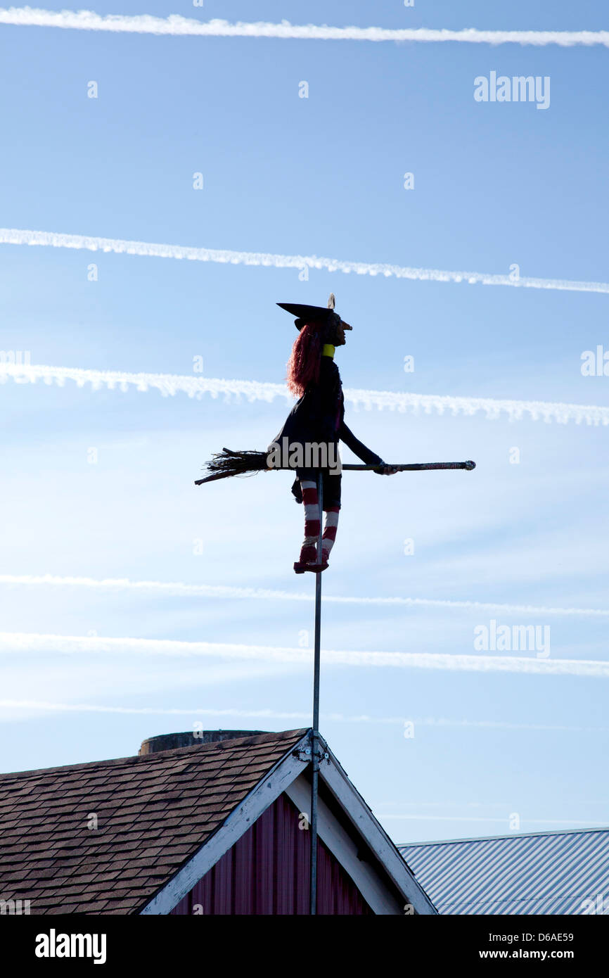 Sorcière et balai sur Pole attaché à Barn Roof avec sentiers de l'avion dans le ciel Banque D'Images