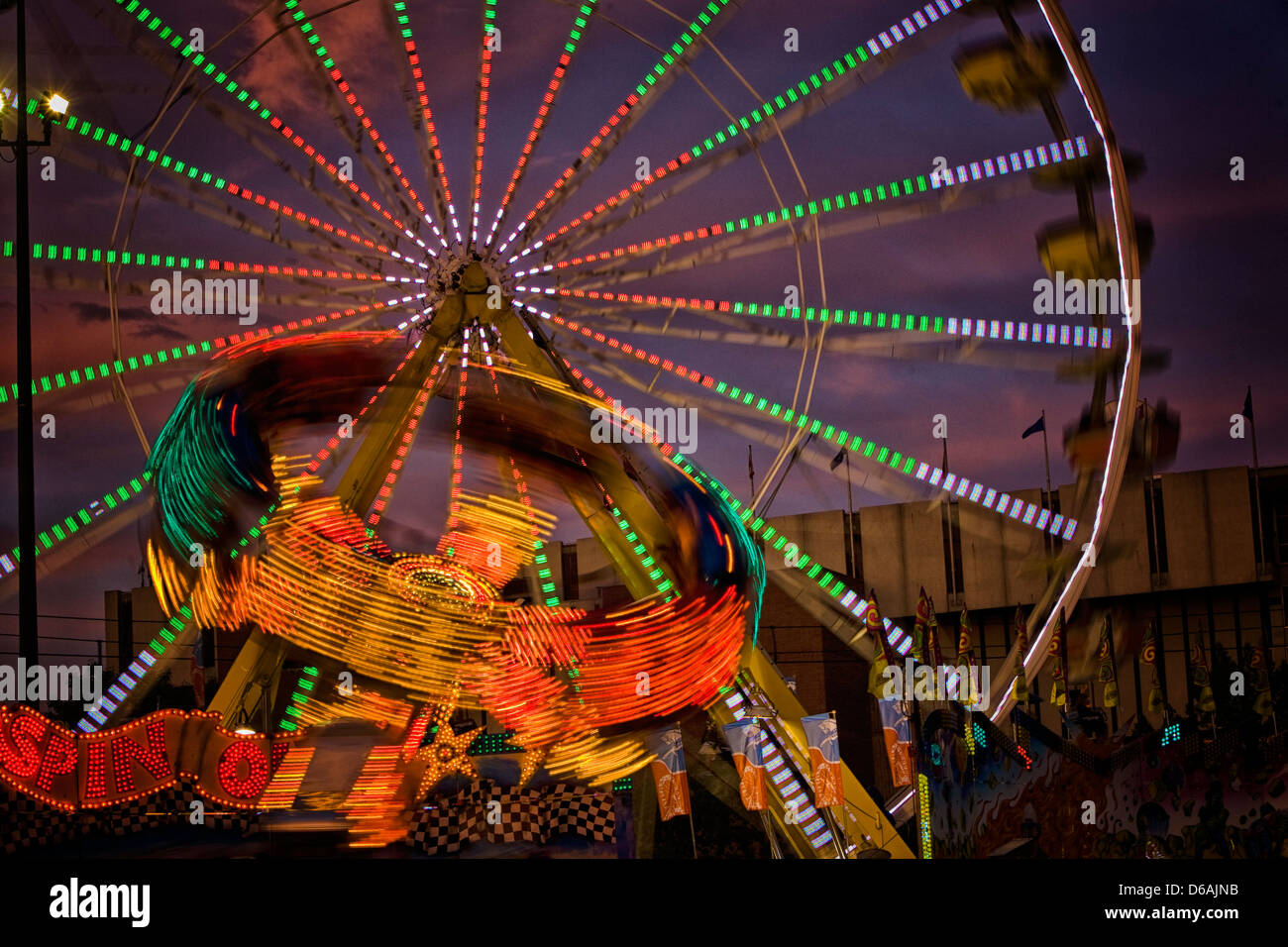Spin Out, un manège de nuit avec grande roue derrière elle, photographiée de nuit avec une longue exposition montrant le motion blur Banque D'Images
