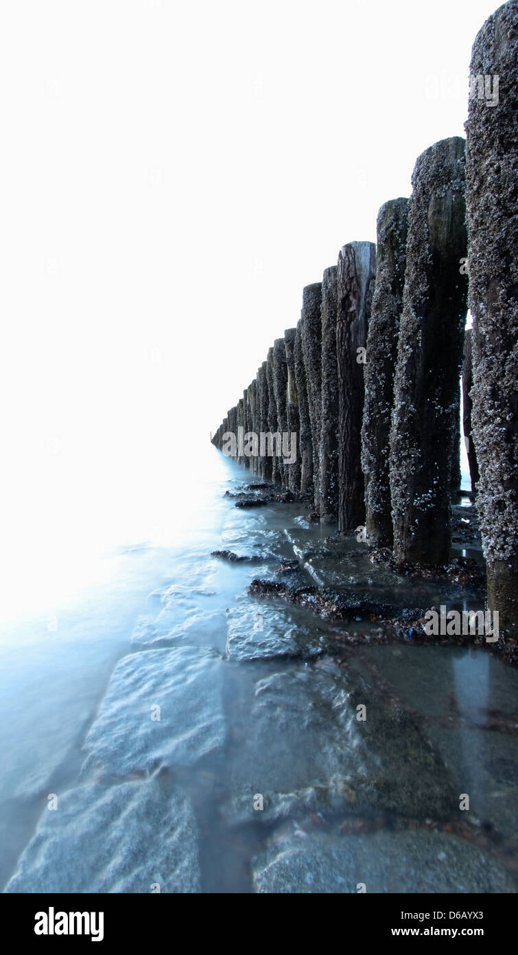 L'exposition longue sur la plage, avec de l'eau sur les pierres et cailloux des bâtonnets de bois. Il est construit pour briser les vagues. Banque D'Images