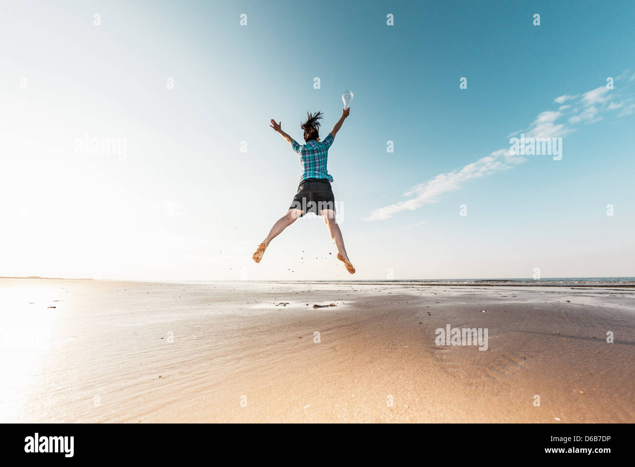 Woman jumping with Light bulb on beach Banque D'Images