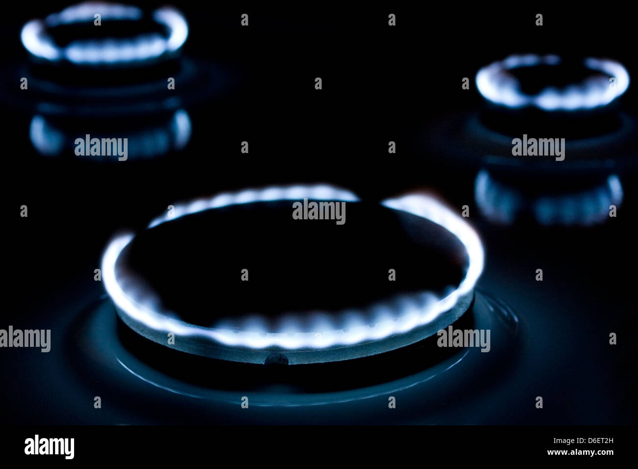 Photographie de trois plaques de cuisson à gaz, avec les flammes bleues brillants dans l'obscurité. Banque D'Images