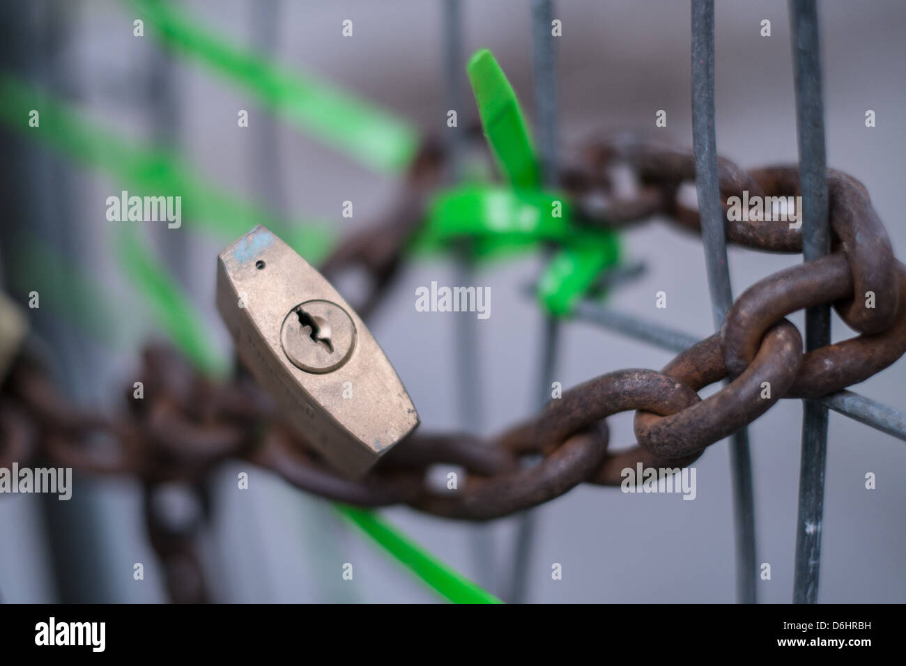 Chaîne rouillée enroulée autour d'une clôture métallique fixée avec des attaches mono-vert et un cadenas en laiton Banque D'Images