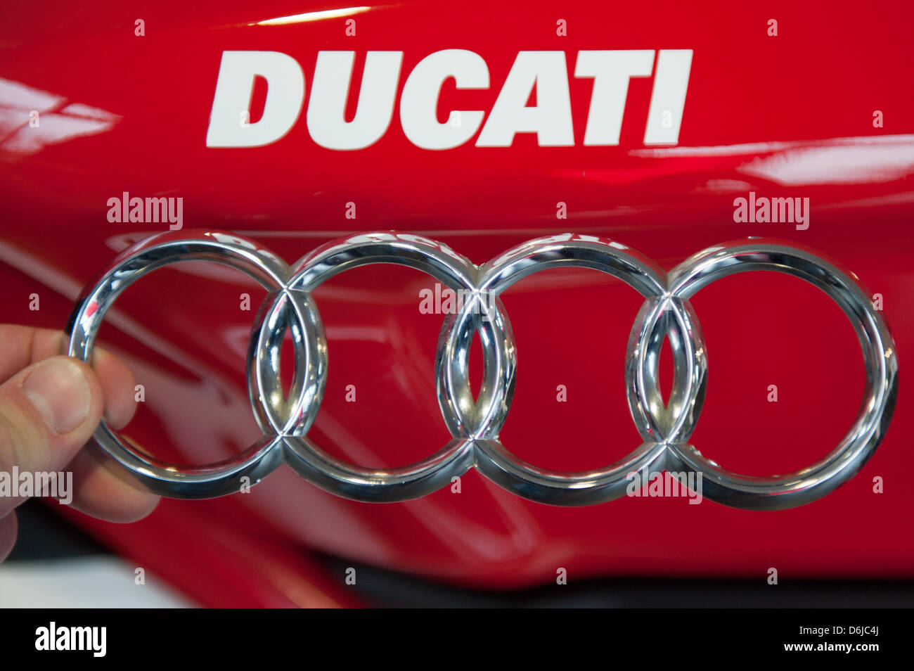 L'illustration montre une main tenant les quatre anneaux Audi en face d'un lettrage Ducati à Regensburg, Allemagne, 13 mars 2012. Le constructeur automobile allemand Audi s'intéresse au fabricant de moto ducati. Les négociations concernant l'achat sont en cours. Photo : Armin Weigel Banque D'Images