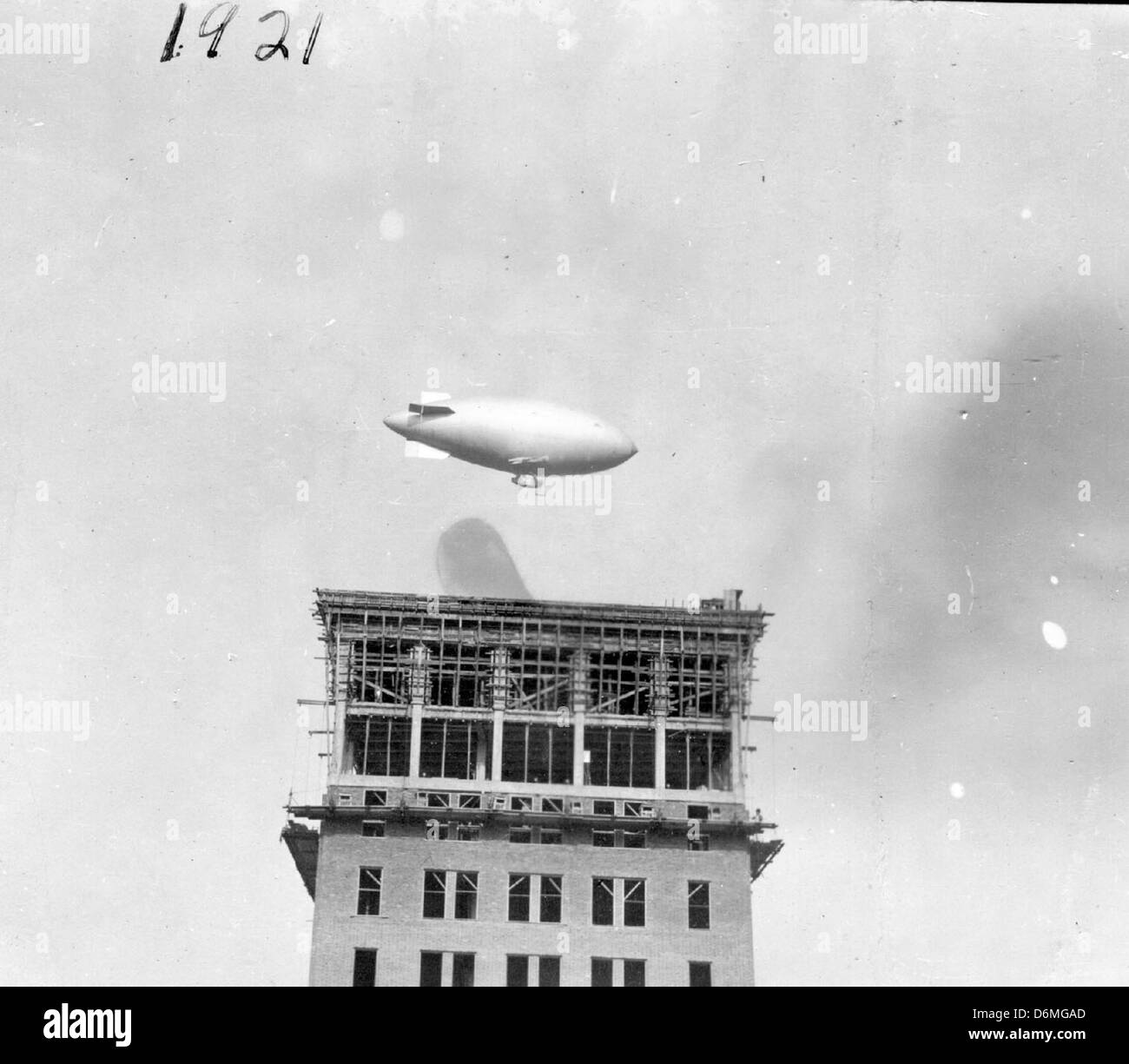 Cette photographie capture un blimp survolant le bâtiment associé au célèbre vol de l'aviateur Clark. L'année 1920 marque une période significative dans les débuts de l'histoire de l'aviation, mettant en évidence l'essor des dirigeables dans l'aviation commerciale et militaire. Banque D'Images