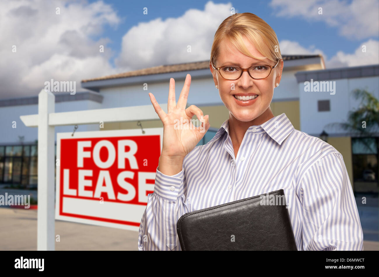 Smiling Businesswoman with Okay signe devant un immeuble de bureaux vacants et pour location enseigne immobilière. Banque D'Images