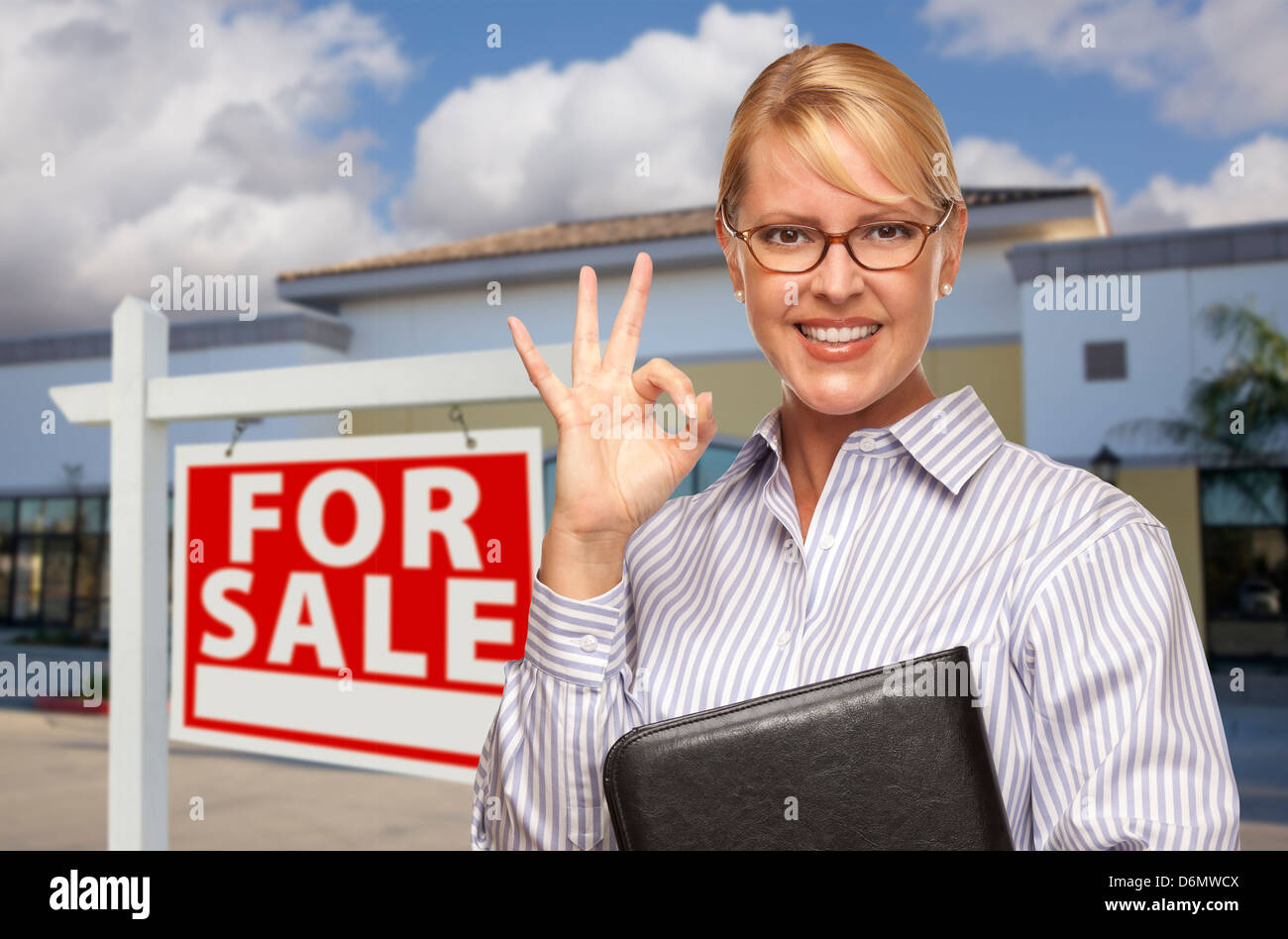 Smiling Businesswoman with Okay signe devant un immeuble de bureaux vacants et achat immobilier signe. Banque D'Images