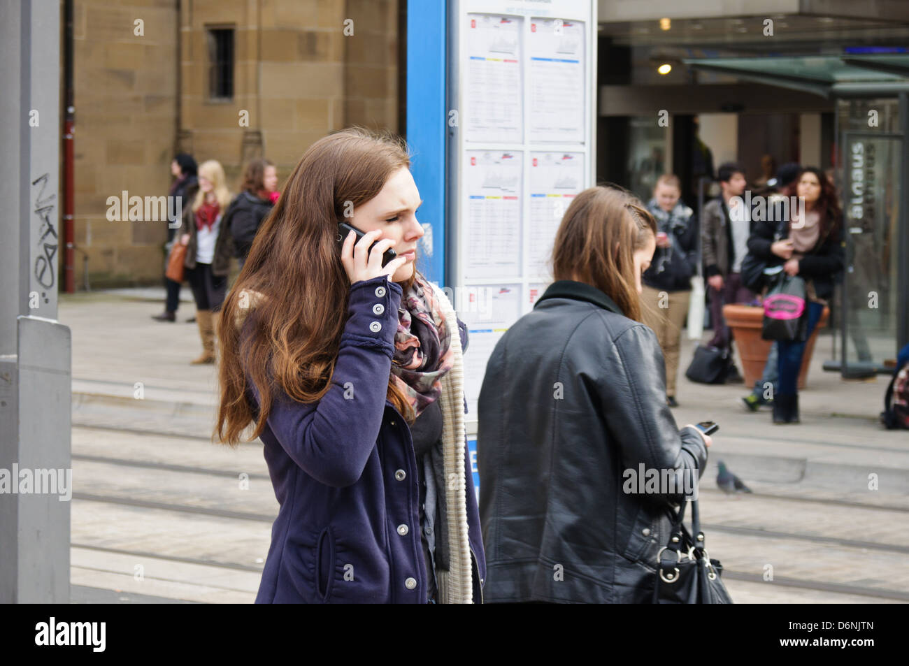 2 Les jeunes femmes de race blanche à l'aide de leurs téléphones intelligents, en attendant à un arrêt de bus, tram station - Heilbronn Allemagne Banque D'Images