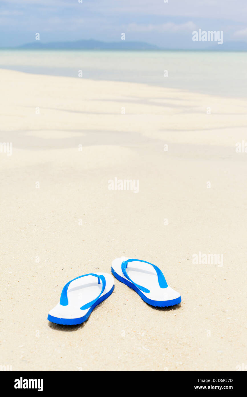 Tongs bleu sur l'idyllique plage de sable blanc, très peu de profondeur de champ. Banque D'Images