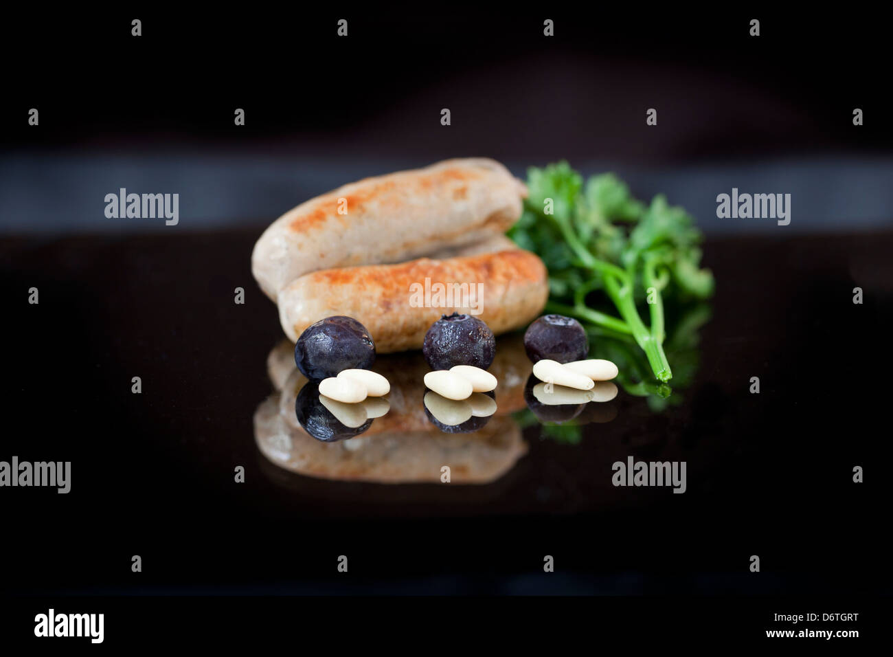 Anglais gastronomique les saucisses avec les bleuets, les noix de pin et le persil présenté sur un plat noir Banque D'Images