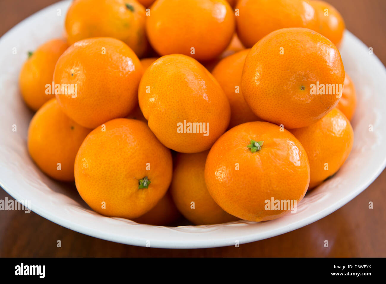 Oranges, clémentines une variété de mandarine, Citrus reticulata, dans un bol blanc, assis sur une table en bois. Libre. Banque D'Images