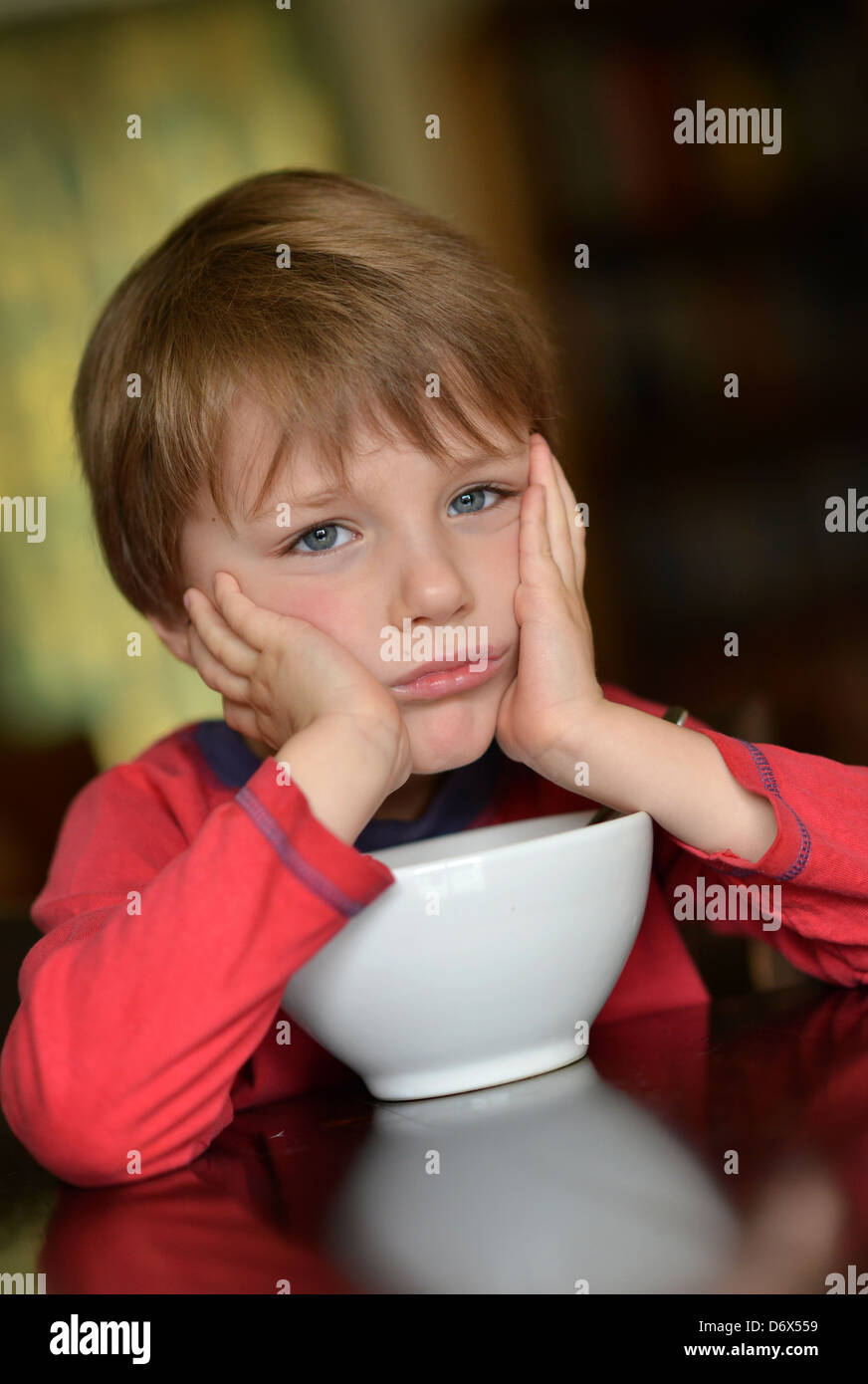 Un garçonnet de cinq ans avec les cheveux bruns et les yeux bleus de manger un bol de céréales pour son petit-déjeuner. Banque D'Images