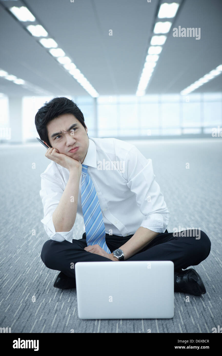 Stressed businessman assis sur le plancher d'un bureau vide avec un ordinateur portable Banque D'Images