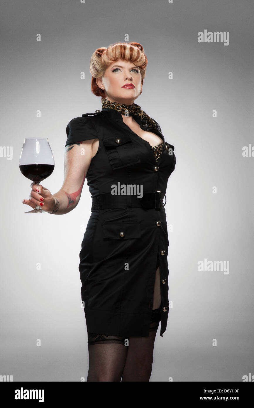 Portrait de pin-up girl tatouée, tenant un grand verre de vin rouge Banque D'Images