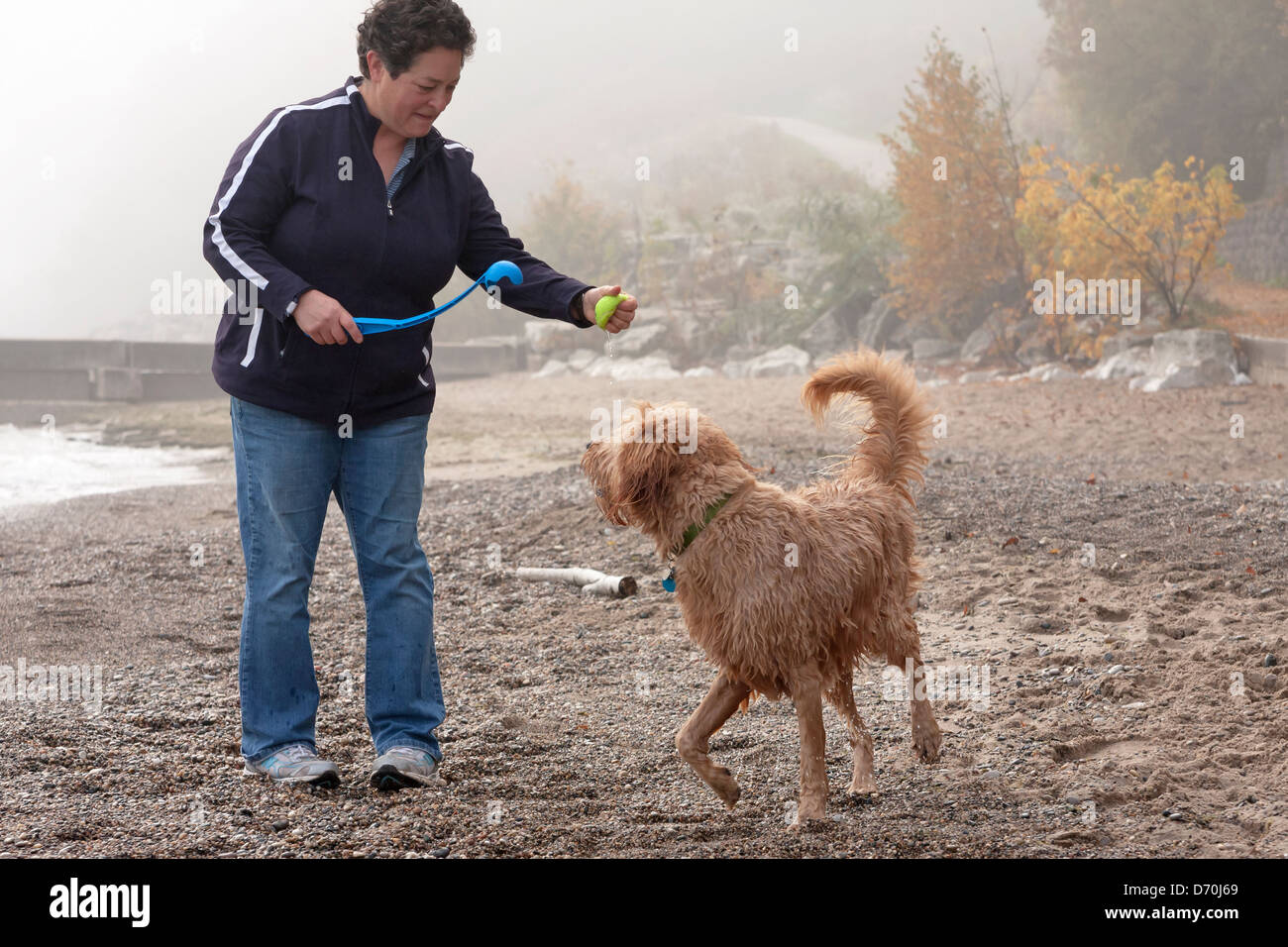 Une femme se prépare à lancer une balle à son chien sur une plage du lac Michigan en automne. Banque D'Images