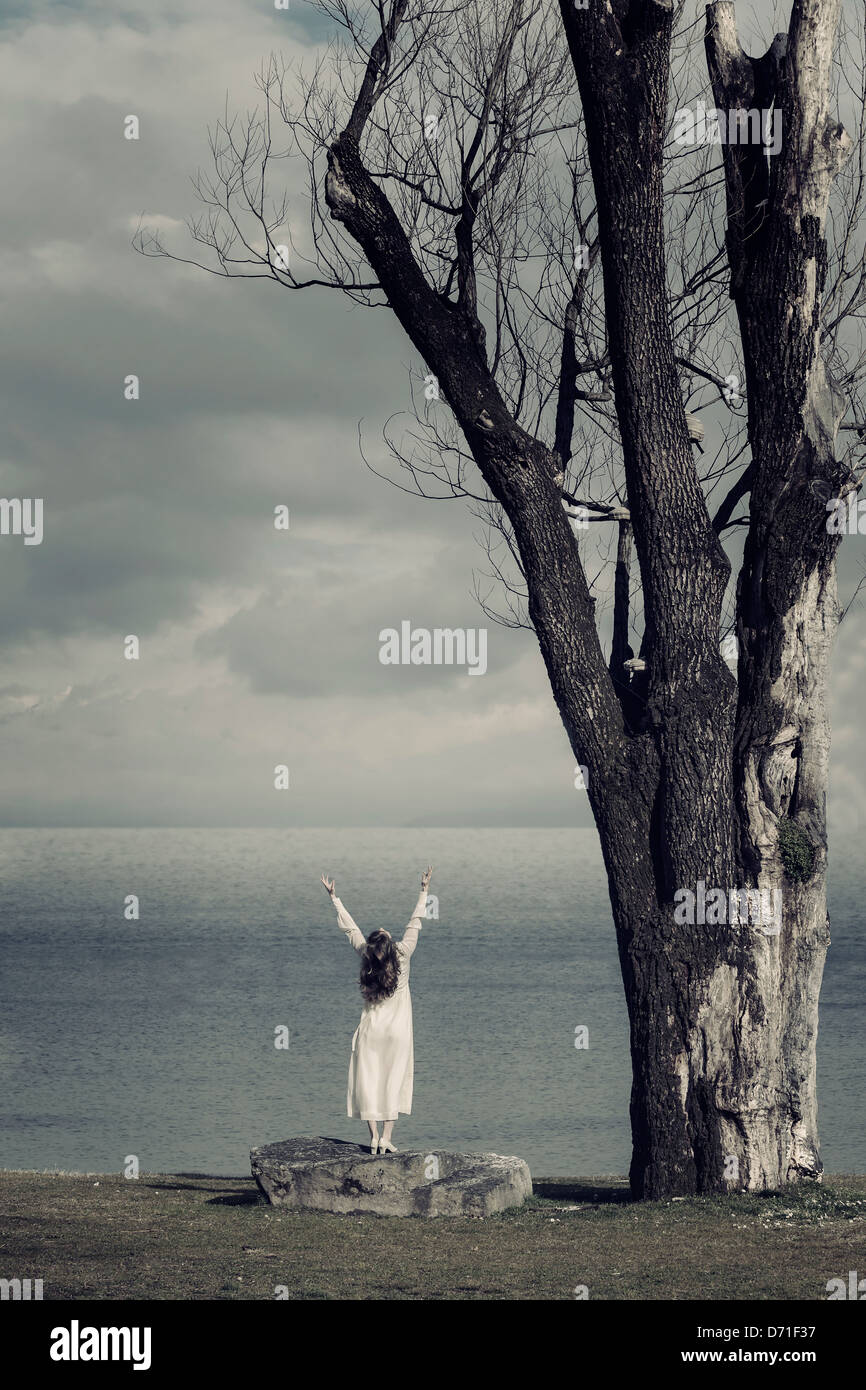 Une jeune fille en robe blanche est debout sur une pierre à la mer Banque D'Images