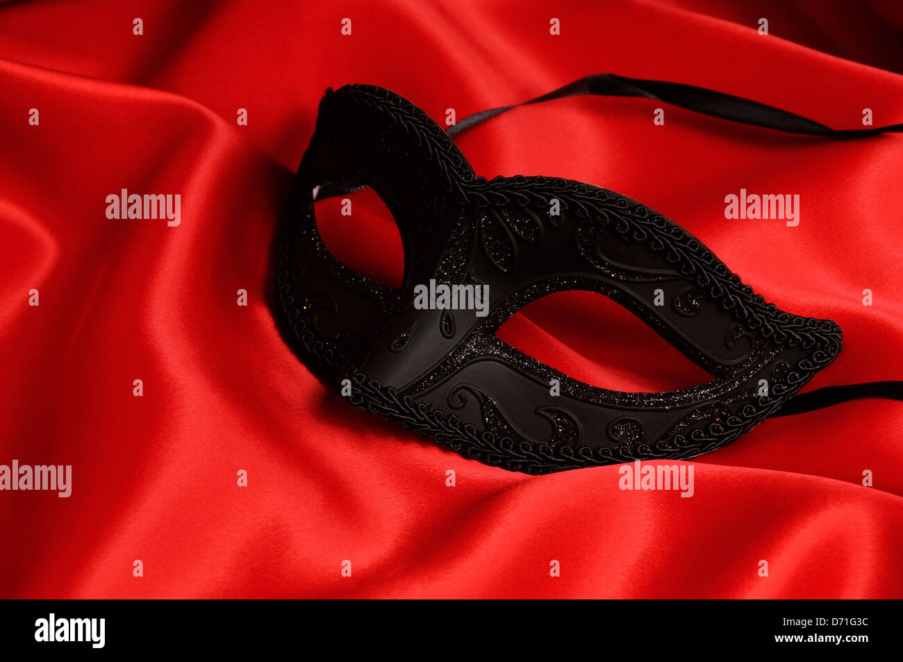 Masque noir sur fond de satin rouge. Banque D'Images