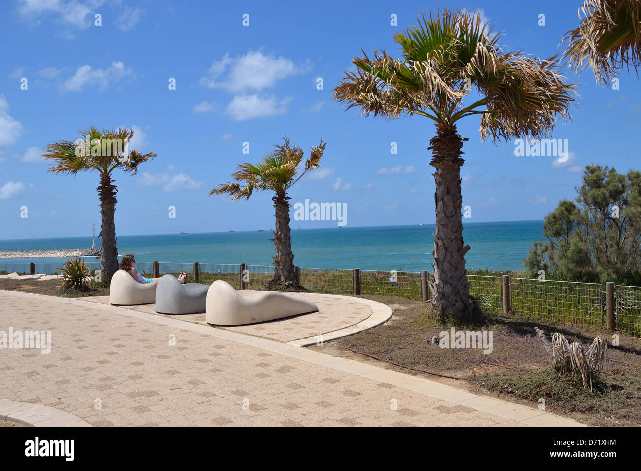 Une jeune fille assise sur une chaise de détente sur la promenade d'Ashkelon, en Israël. Banque D'Images