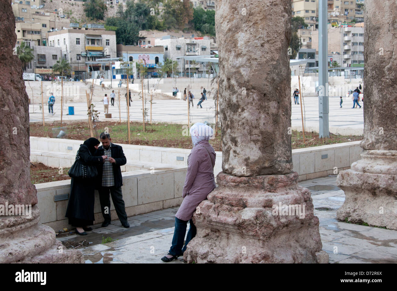 La Jordanie, Amman. Amphithéâtre romain. Fille pose à ses parents par une colonne romaine tandis que les jeunes jouent au football dans l'arrière-plan Banque D'Images