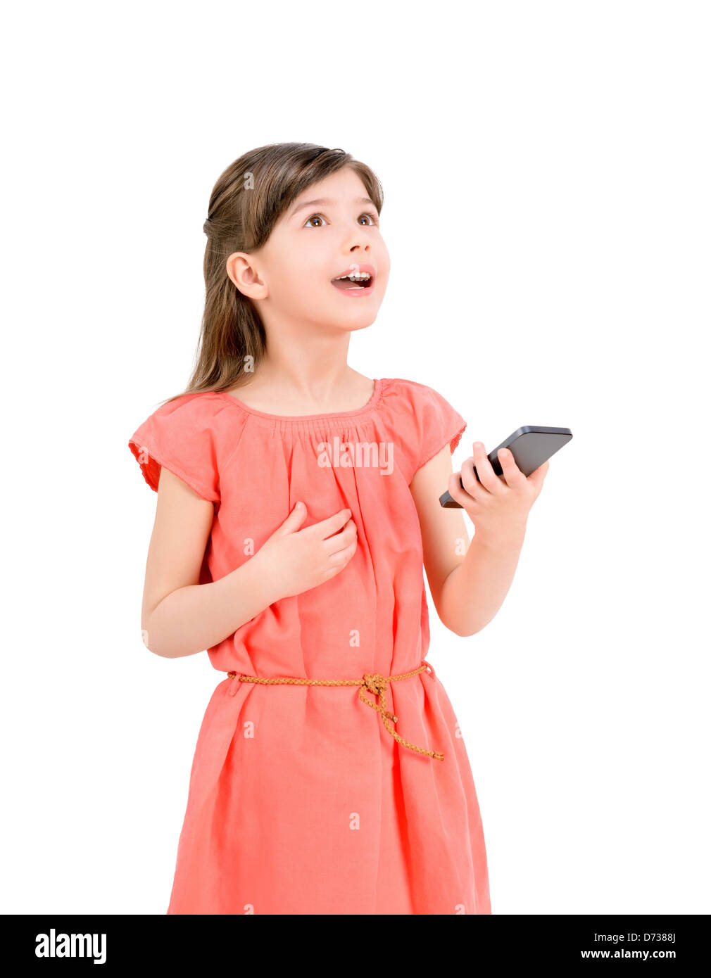 Inspiré cute little girl in red dress looking up et tenant à la main un téléphone mobile. Isolé sur fond blanc. Banque D'Images