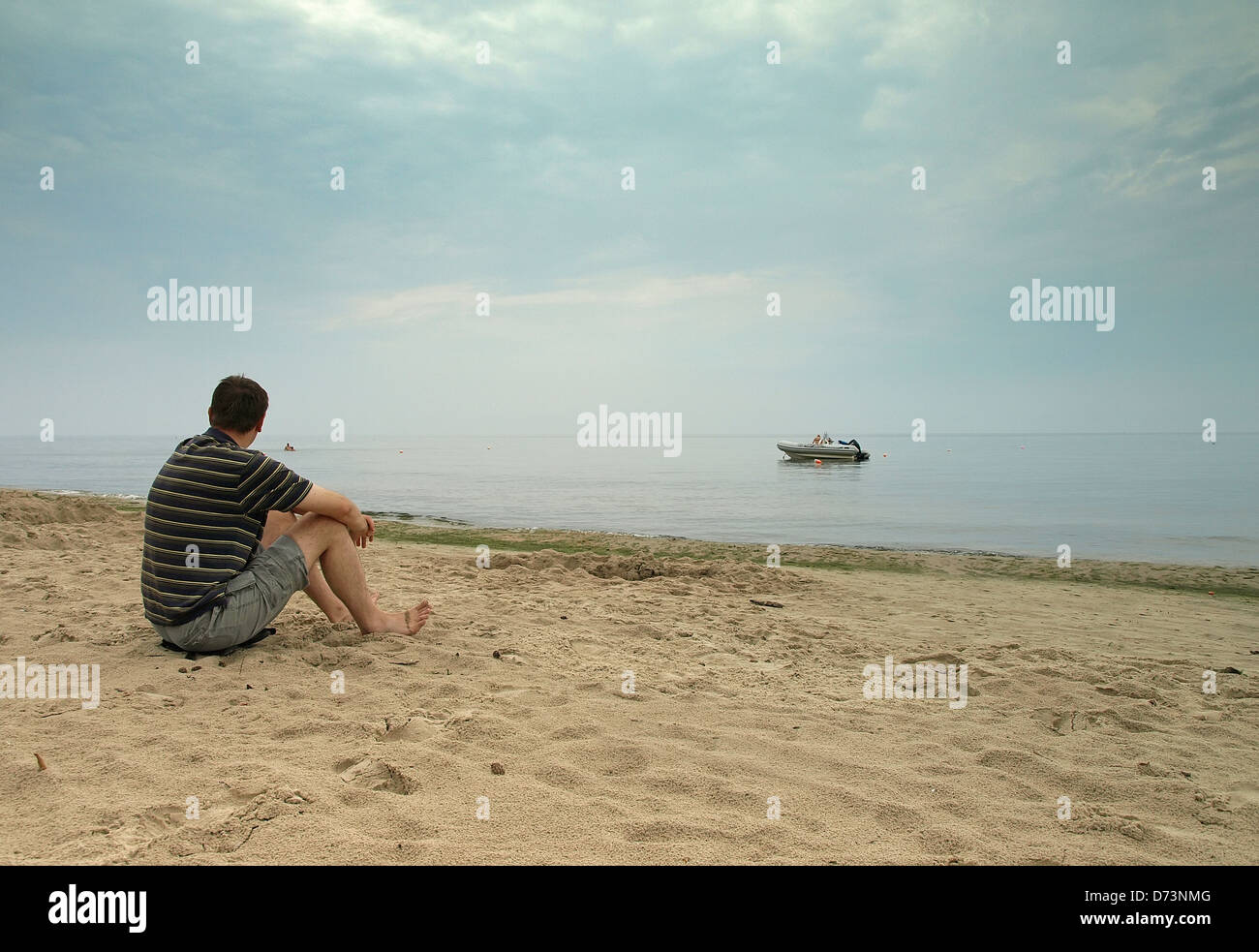 Un homme assis sur la plage et à la recherche à la voile Banque D'Images