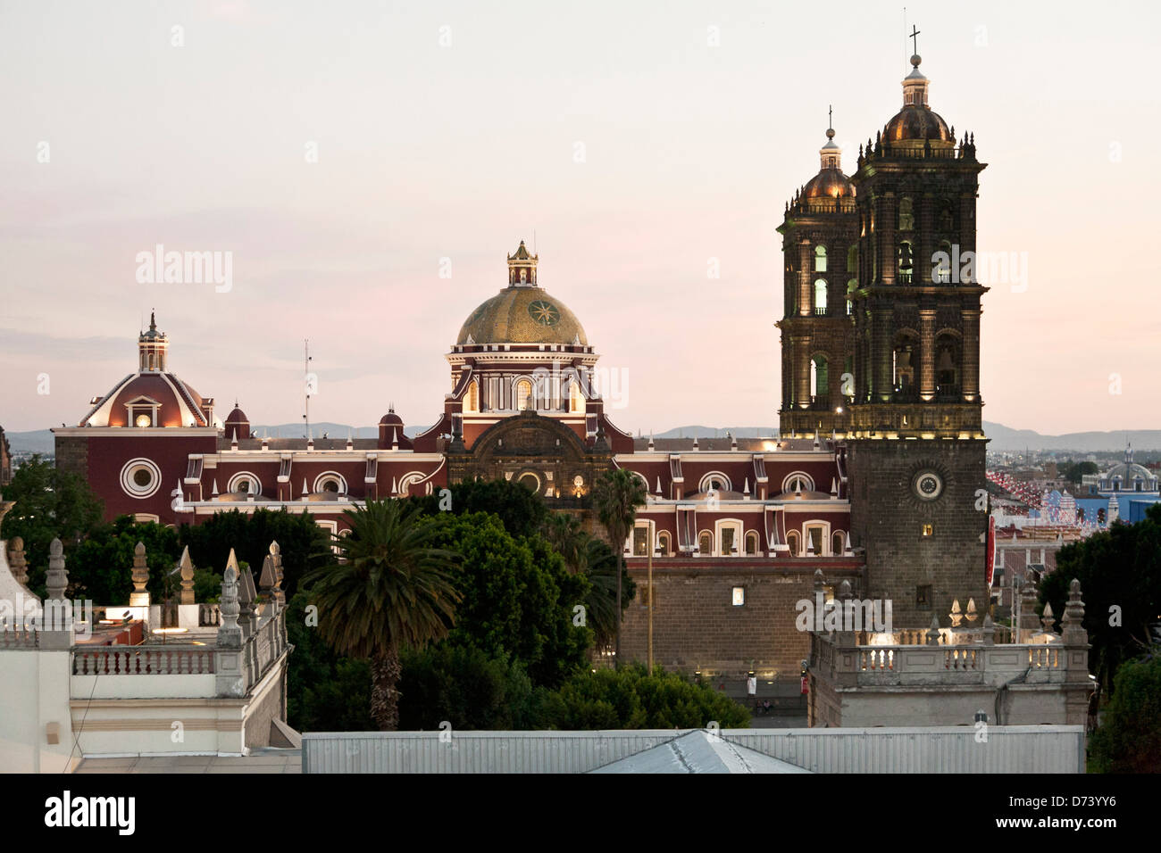 Vue latérale avec un dôme d'or et les clochers de la cathédrale de Puebla vu au-dessus des arbres de Zocalo dans twilight glow contre ciel rose allait au Mexique Banque D'Images