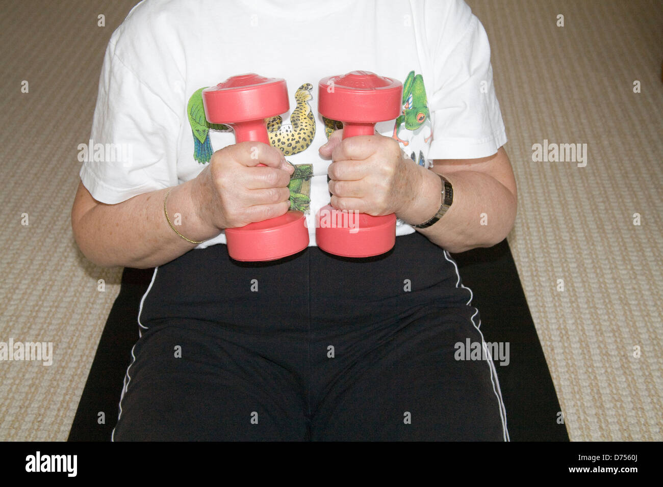 UK woman sitting on exercise mat à l'aide de poids rose à l'exercice des armes à accroître la flexibilité et la capacité pulmonaire Banque D'Images