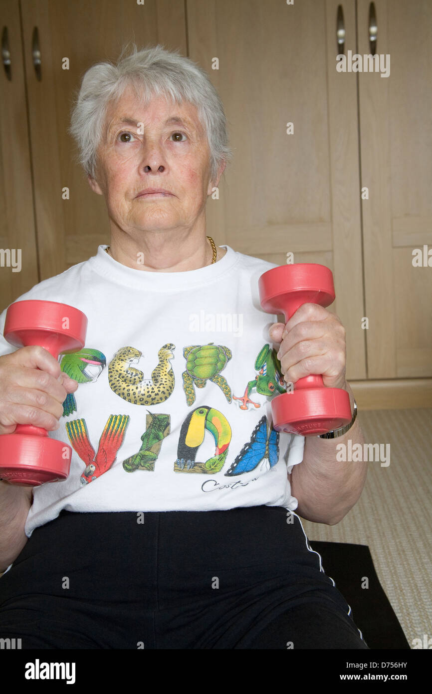 UK woman sitting on exercise mat à l'aide de poids rose à l'exercice des armes à accroître la flexibilité et la capacité pulmonaire Banque D'Images