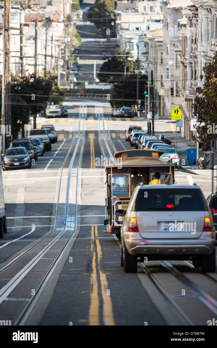 Cable car Steep Street San Francisco // SAN FRANCISCO — Un téléphérique et une voiture parcourent l'une des rues escarpées de San Francisco, avec les pistes du téléphérique directement intégrées dans la chaussée. Le système de téléphérique, qui a commencé à fonctionner en 1873, utilise des câbles souterrains pour tirer les voitures de haut en bas du terrain difficile de la ville. Les téléphériques de San Francisco sont parmi les rares systèmes de téléphériques à commande manuelle encore en fonctionnement régulier dans le monde entier. Les pentes abruptes des rues de San Francisco, certaines atteignant des pentes de plus de 30 degrés, ont été un facteur primaire dans le développement Banque D'Images