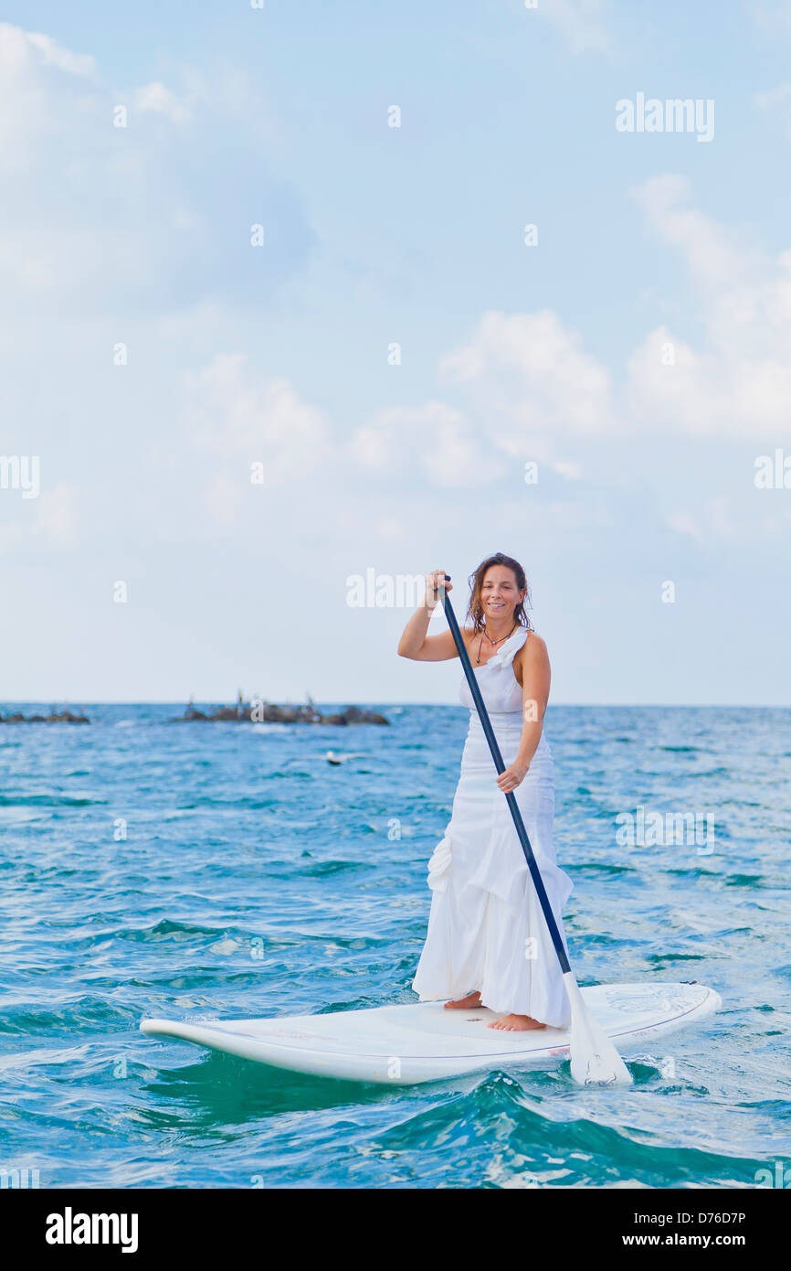 Woman in white dress riding paddle board Banque D'Images