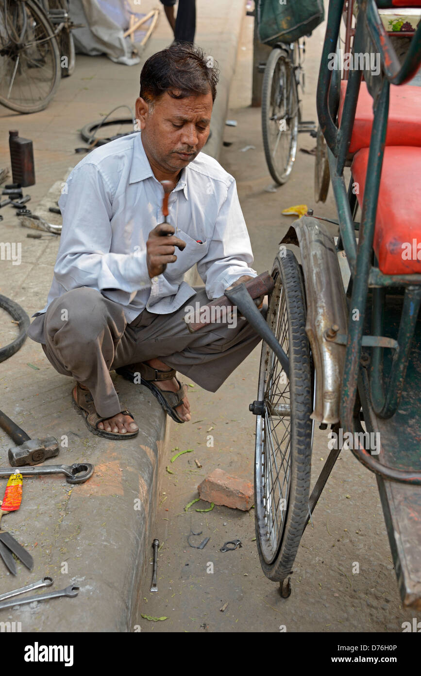 Un pousse-pousse rider la réparation d'une crevaison sur son tube intérieur à un cycle d'atelier de réparation de fortune sur un trottoir dans Old Delhi en Inde Banque D'Images