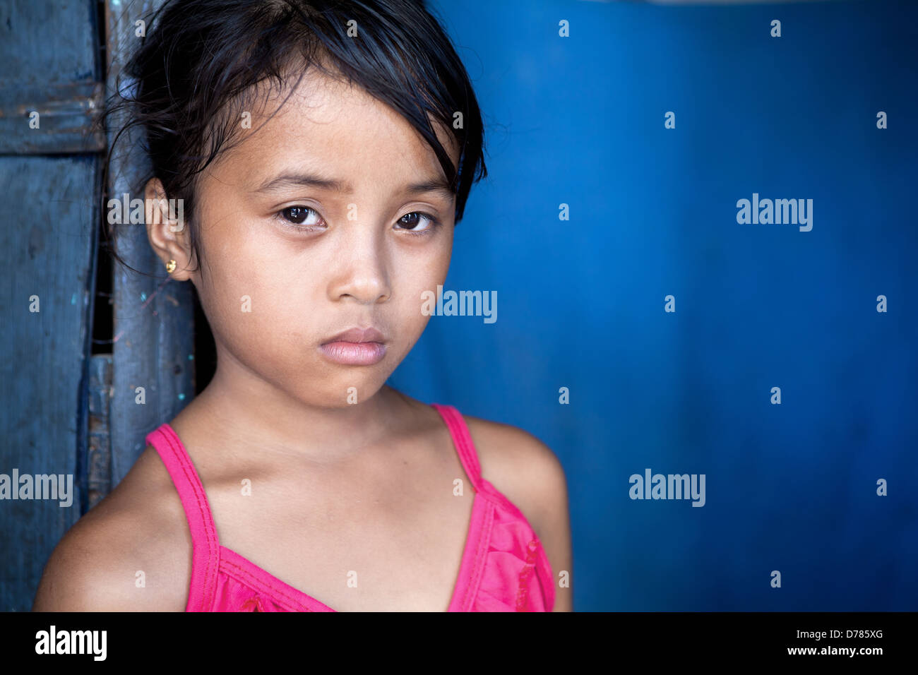 Jeune fille Philippine 8 ans avec l'expression triste et sombre sur le bleu, la pauvreté dans les Philippines. Banque D'Images