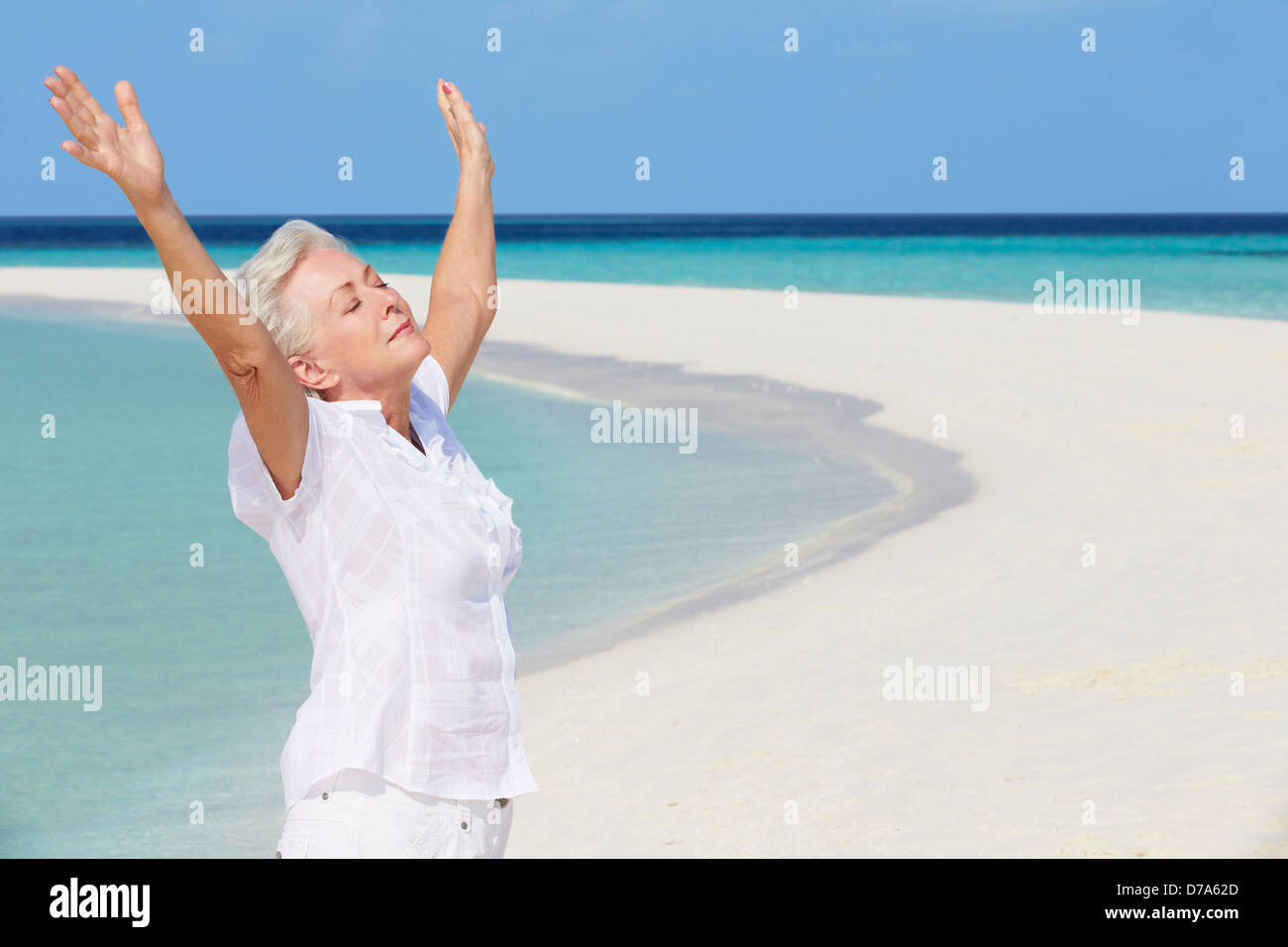 Senior Woman With Arms Outstretched sur Belle Plage Banque D'Images