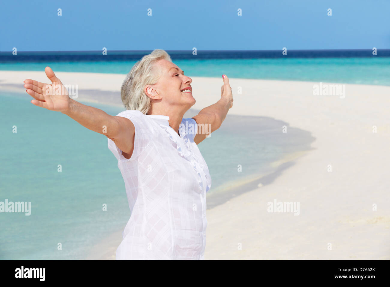 Senior Woman With Arms Outstretched sur Belle Plage Banque D'Images