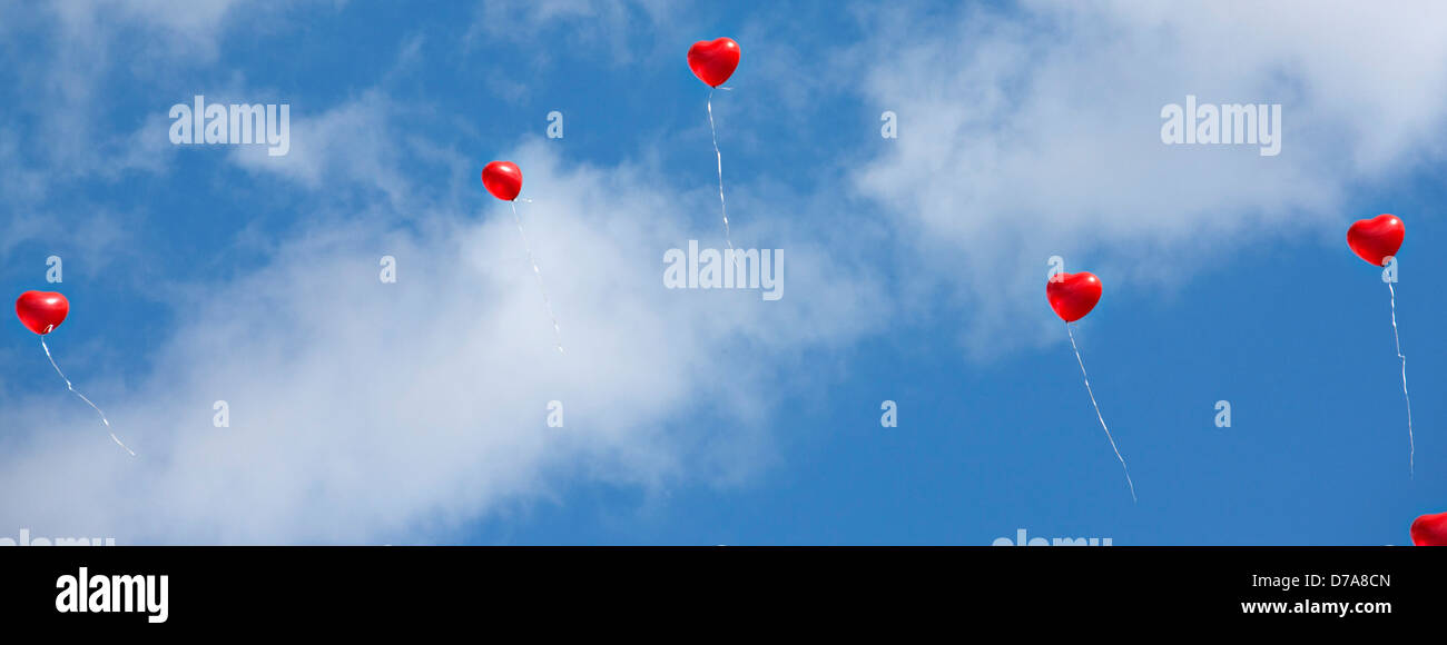 Ballons coeur rouge avec l'air nuageux ciel bleu Banque D'Images