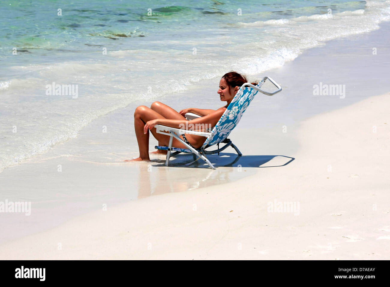 Une jeune femme est assise dans sa chaise pliante en laissant ses pieds ravagé par le surf sur Siesta Key Beach FL Banque D'Images