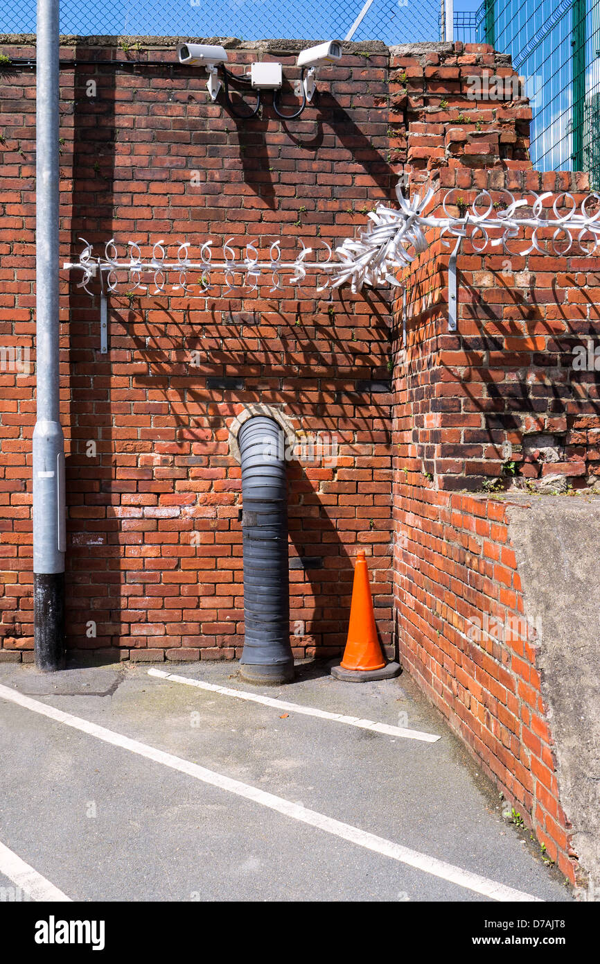 Une image pour illustrer les mesures de sécurité - caméras de vidéosurveillance, d'une clôture à mailles métalliques et un anti-montée, bidules métalliques fixés à un mur. Banque D'Images