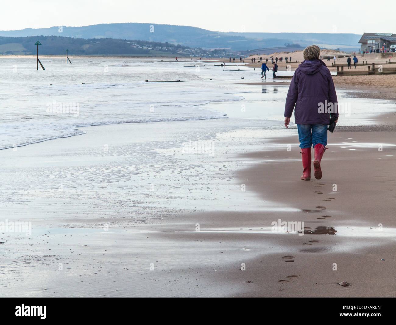 Femme en rouge wellies marcher le long de la plage en hiver d'Exmouth, Devon, Angleterre Banque D'Images