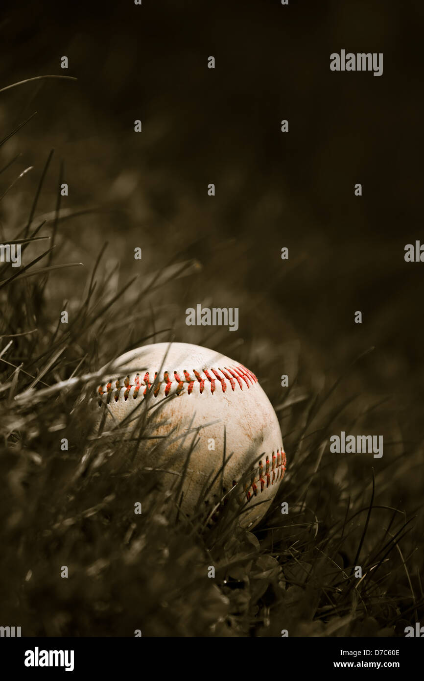 Un vieux et usé grungy baseball assis dans l'herbe verte en sépia. Banque D'Images