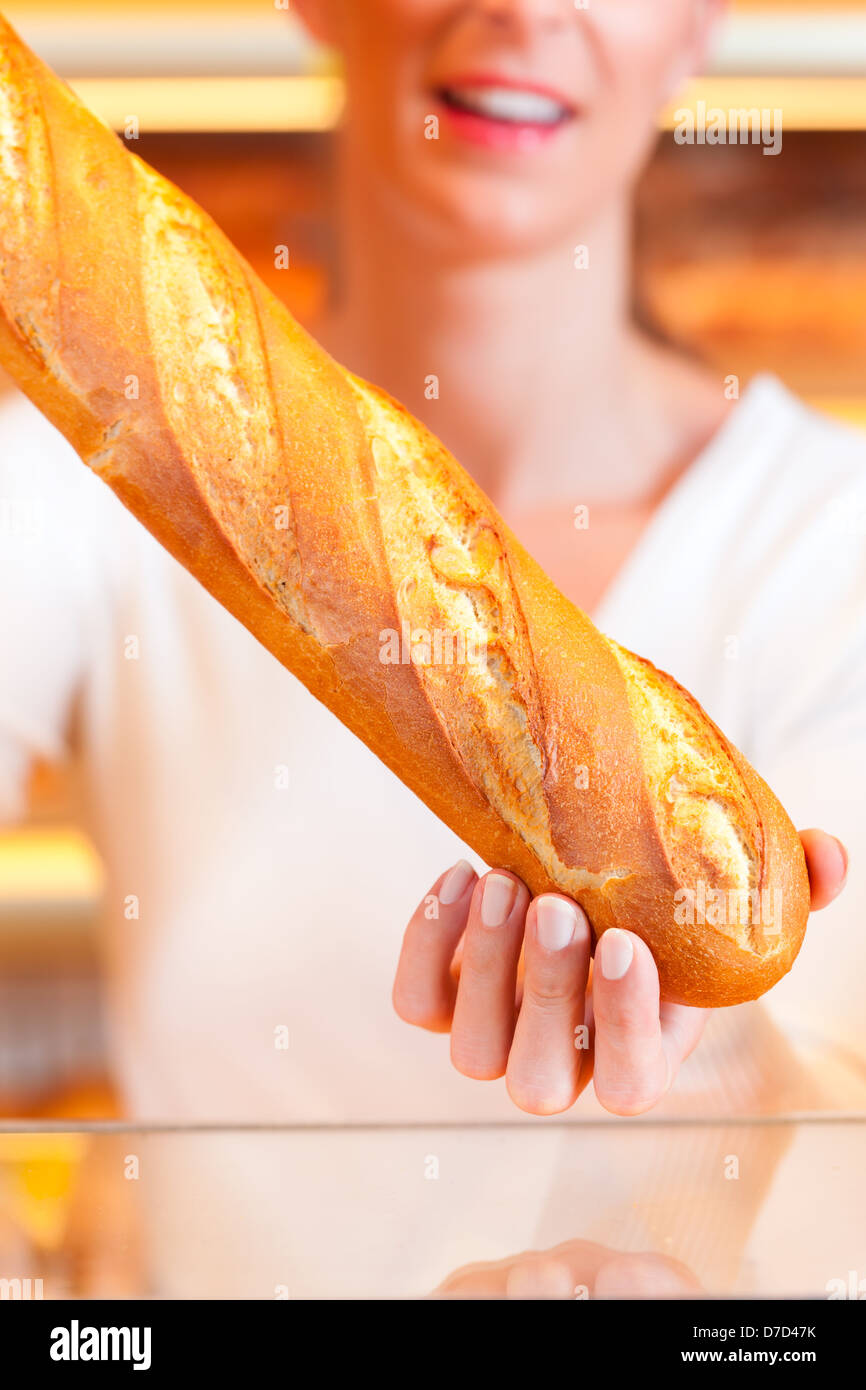 Femme Baker ou vendeuse dans sa boulangerie avec des pâtisseries et produits de boulangerie, une baguette Banque D'Images